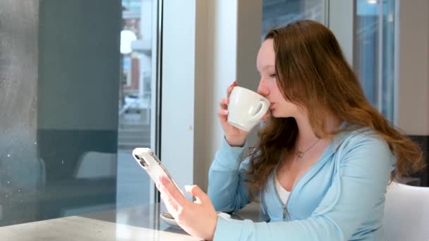 リラックスした女の子コーヒーを飲みながら携帯電話を見て オンラインストアで買い物 高品質4K映像 — ストック動画