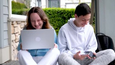 Erkek çocuklar verandada yüksek sesle gülüyorlar sohbet ediyorlar iki telefon el bilgisayarında ev ödevi yapıyorlar spor kıyafetleri giyiyorlar utanç verici spor kıyafetleri giyiyorlar birbirlerine bakıyorlar.