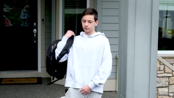 这个男孩把一个公文包放在自己的肩上 正准备去学校 而在这所房子的背景下 私人部门正在四处寻找穿着运动服的青少年 — 图库视频影像