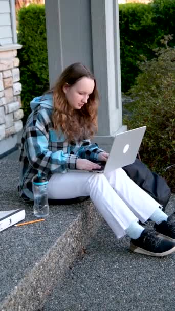 女大学生戴着耳机 坐在室外在线学习的楼梯上 远程学习虚拟课程 观看网上远程课程收听播客 — 图库视频影像