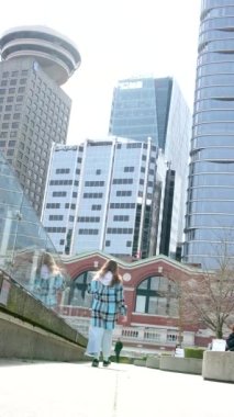 Genç kız arka planda büyük cam binaların gökdelenlerine karşı sedyede yürüyor. Kız uzakta duruyor ve Vancouver Canada Place Liman Merkezi 'ne bakıyor.