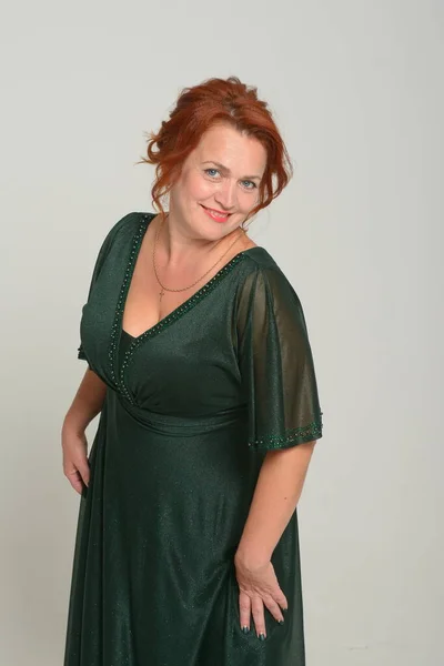 グレーの壁の背景に腕を組んで立って緑のドレスを着たかなり赤毛の若い女性のイメージ 見るカメラ女性赤毛緑のドレス — ストック写真