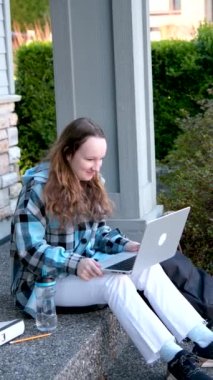 İnternet konferansına katılan genç sarışın kız öğrenci ve karantina sırasında otobüs durağında konferans dinliyor. Yüksek kaliteli FullHD görüntüler