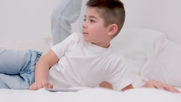 6歳の少年は母親とベッドに横になる彼の隣に横になる彼の母親は一緒にケア医療保険穏やかな生活を一緒に時間を過ごすというタブレット家族の快適コールで動作します — ストック動画