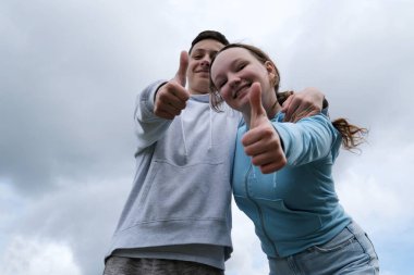 Fırtınalı, bulutlu bir gökyüzü erkeğinin arka planına yaslanmış genç kızlar onaylarını veriyorlar güzel çocuklar için sosyal yardım sosyal hizmetler okulu reklamları yapıyorlar.