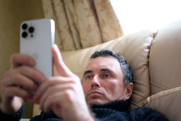 İphone 13 Pro Max 'i kullanan bir adam, bulanık bir şekilde yatağa uzanmış, elinde telefonuyla dinleniyor rahat bir şekilde uzanıyor.