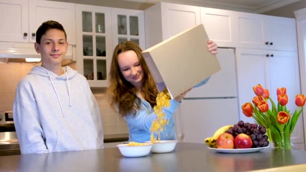 10代の男の子と女の子の料理朝食は ボックス上のシリアルの箱から注がれましたテキストスペースのためのあなたの広告空のスペースおいしい食べ物は楽しい兄弟姉妹と一緒に時間を過ごす — ストック動画