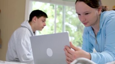 Ergenlik çağındaki ablalar okulda online okuyorlar. Aynı odada dizüstü bilgisayarın yanında oturuyorlar. Parlak bir oda. 