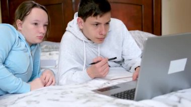 Çevrimiçi öğrenim gören gençler dizüstü bilgisayarın yanında oturup ödev yapıyor ve film arkadaşları seyrediyor sınıf arkadaşları yatak odasında birbirleri gibi gülümsüyor 