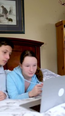Çevrimiçi öğrenim gören gençler dizüstü bilgisayarın yanında oturup ödev yapıyor ve film arkadaşları seyrediyor sınıf arkadaşları yatak odasında birbirleri gibi gülümsüyor 