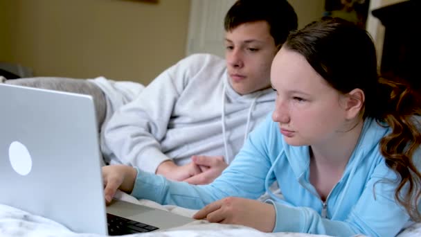 オンライン学習ティーンエイジャーの男の子と女の子がノートパソコンの近くに座って 映画の友人を見て宿題をやってクラスメイトベッドルームの笑顔お互いに最初の愛 — ストック動画