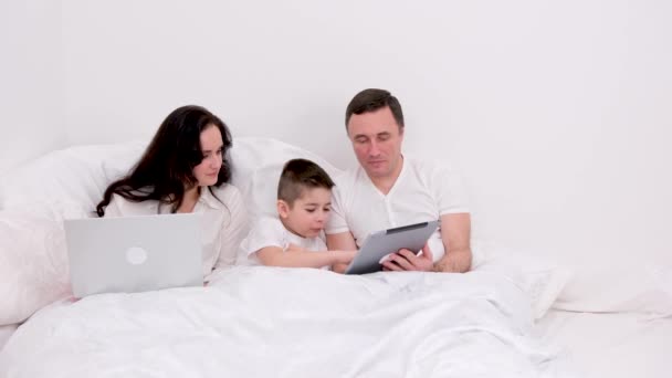 男人女人男孩一起在床上度假聊天玩得开心放松看平板电脑真人真事在家里谈恋爱快乐在小工具上的成功在广告文本上快乐的家庭 — 图库视频影像