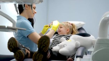 Genç doktor dişçi koltuğuna ilk kez mutlu bir şekilde gülümsüyor. Hoş sohbetler. Süt dişleri, süt dişleri, sarı saçlı kız çocuk muayenehanesi.