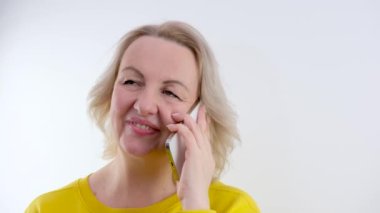 Genç, beyaz bir kadın, parlak sarı bir arka planda akıllı telefonuyla yazı yazıyor. Yüksek kalite 4k görüntü