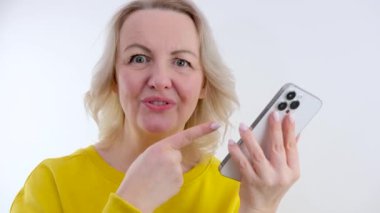 Sarışın, başparmağını kaldırmış, telefon reklamında başka bir parmak daha gösteriyor. Gülümse, dans et. Bir çok hoş duygu kadının elinde telefonla.