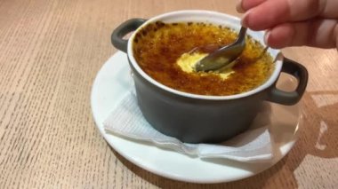 creme brulee tatlıları kaşıkla toplanır. Beyaz bir tabakta beyaz bir tencerenin üzerinden yanmış şeker kırılır.