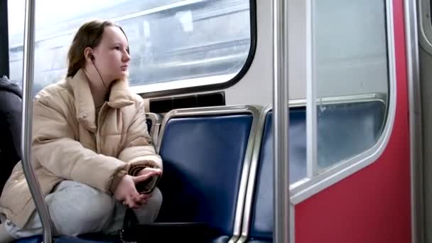 少女乘火车乘火车乘火车坐公共汽车耳机听音乐秋天春天冬天暖米黄色的夹克头发系在真正的人的腿上抱着悲伤的梦在等待停止 — 图库视频影像