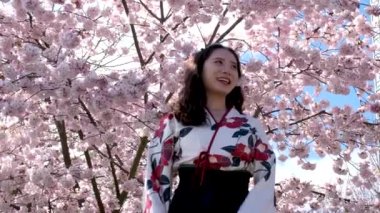 Arka planda sakura çiçekleri olan genç ve güzel bir kadının portresi. Dışarıdaki kameraya bakan güzel bir kadın. Çiçek açan elma ağaçlarındaki kadın.
