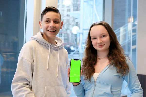 stock image Young millennial friends sitting outside with coffee and looking at green screen phone in park. Happy smiling people using modern smartphone technology. Media, lifestyle, internet education