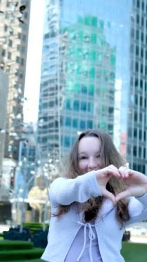 Güzel kız ellerini gökdelenlere ve büyük şehirlere karşı kaldırarak kalbini gösteriyor. Kocaman cam binaları olan New York New York Kanada Vancouver Toronto düz saçlarını rahatlat. Gülümse.