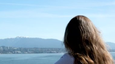 Güzel bir reklam kızı elinde kamerayla dağlara bakıyor. Uzun saçlı, mavi saçlı, yazı turizmi için arka plan alanı olan bir okyanus kadını. Vancouver Canada 'ya seyahat et.