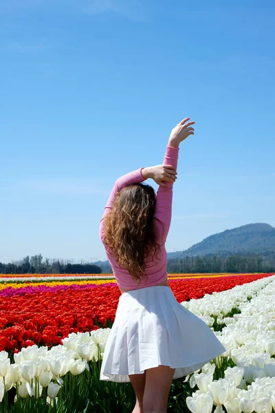 beauty young girl tiptoeing through tulips across field space for text vertical video clear sky mountains in distance exhibition of tulips purity freshness white skirt pink blouse snow-white flowers