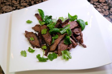 Kızarmış domuz eti, sarımsaklı ve biberli, beyaz bir tabakta yemeye hazır. Yüksek kaliteli fotoğraf. Yeşillik tabakta lezzetli kızarmış et servis edilmeye hazır.