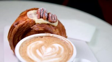Lokantada nefis bir tatlı, beyaz tabakta yuvarlak kruvasan, cevizli ve kremalı pasta, vanilyalı kouign Amann yuvarlak kruvasan, New York Roll, tarçınlı tarçınlı latte.