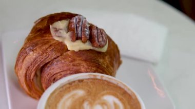 Kafedeki masada kapuçino ve kruvasan var. Sabah güneş ışığı masanın üzerine düşer. Güzel gölgeler belirir. Nefis kahvaltı, cevizli, vanilyalı, kruvasan ve kahve.