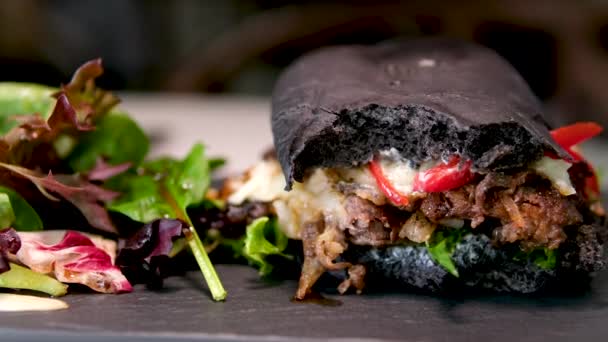 开胃的大三明治三明治汉堡包 上面有黑色的面包 盘子里放着色拉灯 在昂贵的时尚餐厅里四处走动 吃着快餐 手指压在汉堡包上 — 图库视频影像
