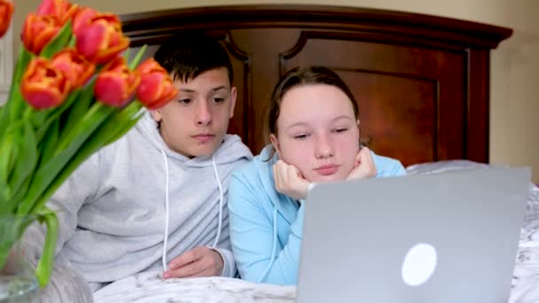 コンピュータの時計映画の近くの部屋のティーンエイジャー一緒に時間を過ごす最初の日良い関係の花はベッドの上の寝室にある快適な雰囲気の学校の子供たちは一緒に宿題をします — ストック動画