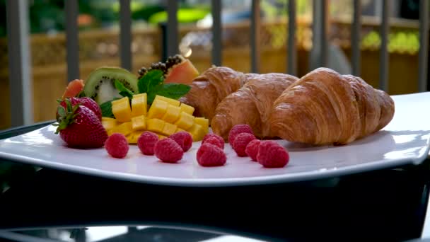 プライベートハウスのバルコニーの巨大な正方形の白いプレート上の美味しいデザートトロピカルサイドフルーツクロワッサン伝統的なフランス語ランチ朝食美味しいサービス美しい料理 — ストック動画