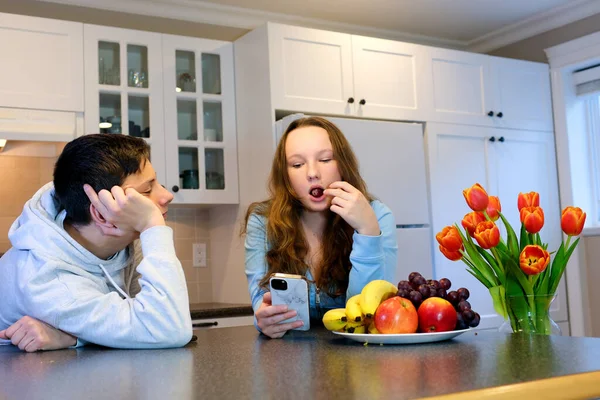 十代の若者たちで台所の少年は目を愛する少女を見て若い女性はブドウを食べる男はテーブルの上に傾きます — ストック写真