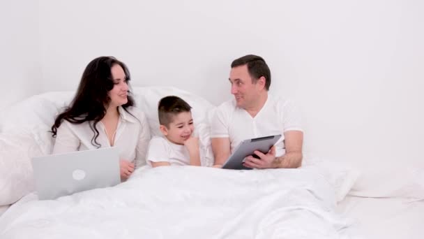 男人女人男孩一起在床上度假聊天玩得开心放松看平板电脑真人真事在家里谈恋爱快乐在小工具上的成功在广告文本上快乐的家庭 — 图库视频影像