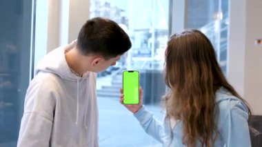 Yeşil ekranlı telefona bakan ve onay veren gençler eğlence tercihlerini doğru yapıyorlar. Beyaz bina duvarlarında bulanık arka planda mesajlaşmak için bizi reklam alanı olarak arayın.