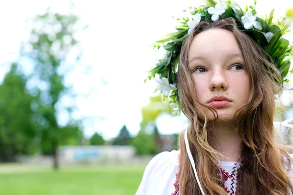 Stock image tender face of young girl in blooming wreath white flowers Green grass Ukrainian national headdress embroidered shirt space for text beauty purity Youth desire to live No war Ukraine Victory Hope