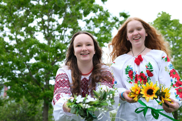 beautiful young girls wearing embroidered shirts laughing smiling putting wreaths on water facing camera stretching out wreaths to us different sunflowers Field flowers girl has red bright sunny hair