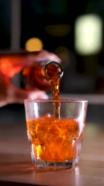 明るいオレンジ色のドリンクアルコールを街を背景に氷の入ったガラスに流し込み — ストック動画