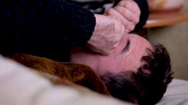满脸胡须的男人在家里躺在靠近气球的沙发上 头疼地醒来 摸着脸 高质量的4K镜头 — 图库视频影像