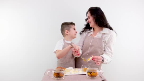 お母さんと小さな息子がチーズハニー朝食に広がる健康食品白背景ドリンクティーキッチンエプロン — ストック動画