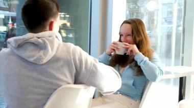 Genç kızlar ve erkekler, kafeteryada oturup sohbet ediyorlar. İlk buluşmada eğleniyorlar. Kafeterya restoranlarında, beyaz bardaklardan kahve içiyorlar.