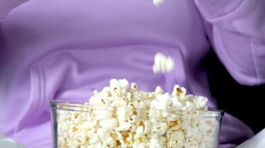 Bir kız cam kaseye patlamış mısır dökerken arka plandaki leylak rengi süveterine yakın plan patlamış mısırı tabağa döküyor. Yüksek kalite 