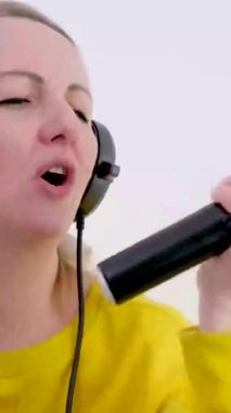 Mikrofonlu yetişkin bir kadın şarkı söyler ve mikrofon karaokesini eğlenceli kulaklıklarla inceler. 