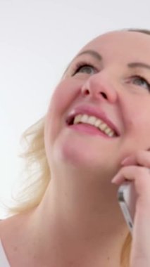 Güzel sarışın kadın cep telefonundan beyaz perdelerin önünde haber başındaki omuzlara gülümseyen bir telefon dinliyor. Yüksek kalite 4k görüntü