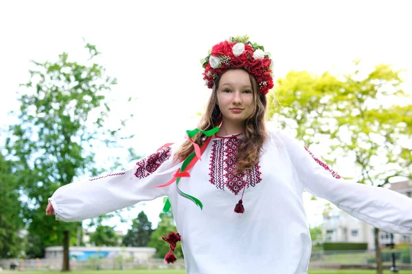 乌克兰美丽的年轻女子 戴着大大的红色花环 头戴亮晶晶的粉色白色红花 美丽的年轻女子 她在吹拂着的头发上编织着辫子 带着丝带 — 图库照片