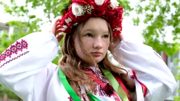 乌克兰美丽的年轻女子 戴着大大的红色花环 头戴亮晶晶的粉色白色红花 美丽的年轻女子 她在吹拂着的头发上编织着辫子 带着丝带 — 图库视频影像