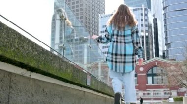 Genç kız arka planda büyük cam binaların gökdelenlerine karşı sedyede yürüyor. Kız uzakta duruyor ve Vancouver Canada Place Liman Merkezi 'ne bakıyor.