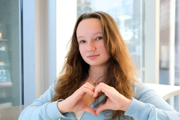 making heart with hands confession choice beautiful teen girl standing by the window holding hands at chest level folding positive sign peace in ukraine