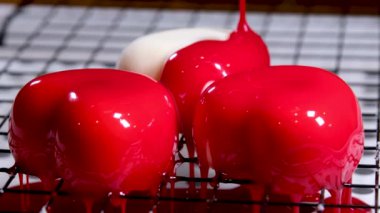 Kırmızı jetle parlak bir kalp şeklinde nefis tatlı kremalı kekler kar beyazı bir tatlı üzerine damlayan bir yükseklikten beyaz bir arkaplanda yemek pişirme sürecine dökülür.