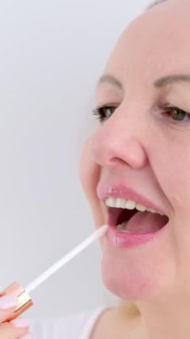 Orta yaşlı sarışın, dudak boyuyor. Parlak bir kadınla. Dudaklarını boyamak için boş bir yere bakıyor. Etkileyici dudaklar. Yüksek kalite 4k görüntü